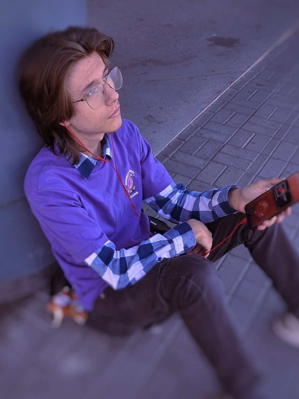 Sitting on the ground outdoors with the player in one hand and wired headphones in.