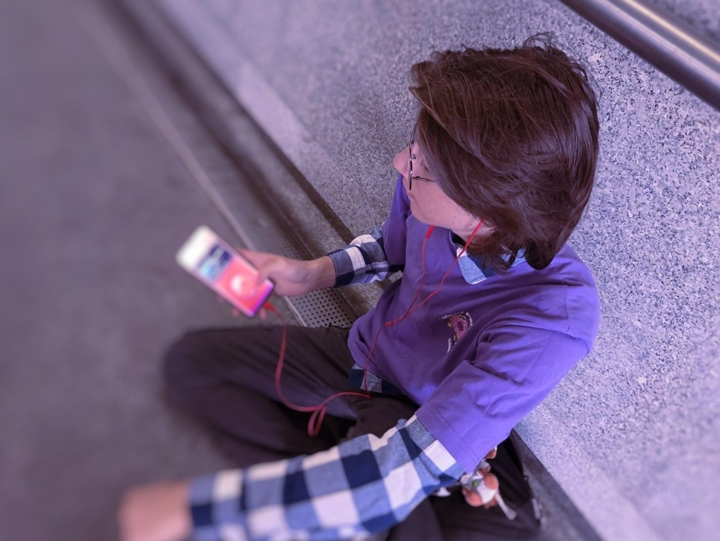 Sitting against a wall in an underpass with wired headphones in, the player showing its red screen.